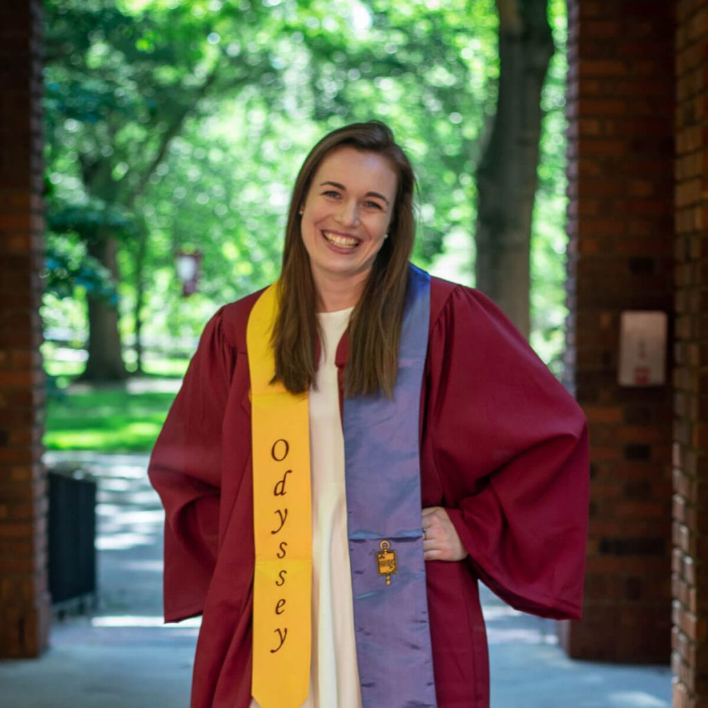 Ashley Jutras posing on Elon's campus in her graduation robe.