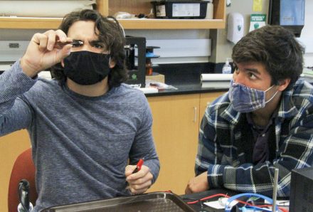 Matthew Del Valle '21, left, examines an LED light before soldering it to a circuit board with the help of Eduardo Gonzalez '21. The pair of engineering majors are designing a camera system that will monitor water turbidity for a constructed floating wetlands, the engineering program's Capstone Project for 2020-21.